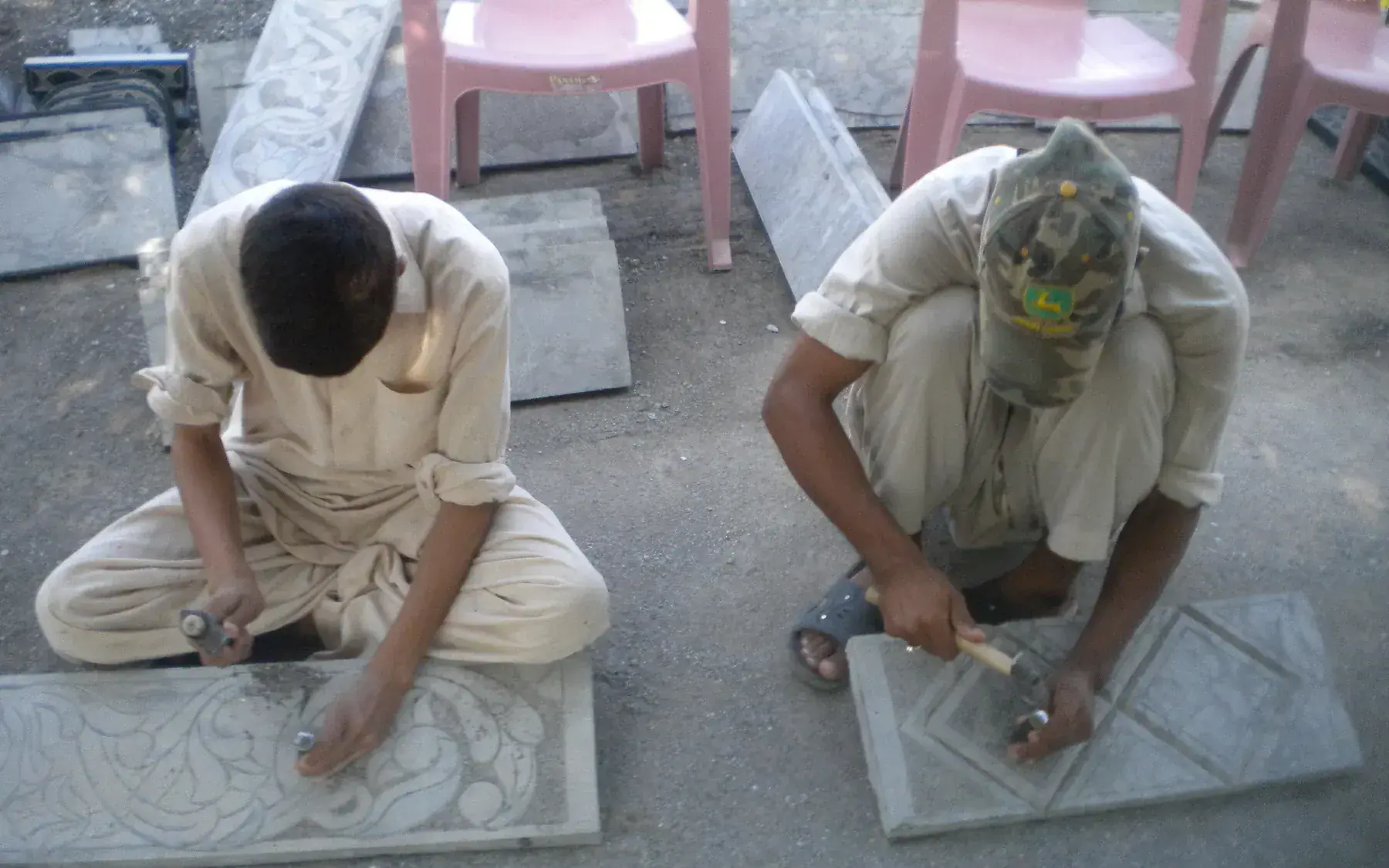 A person crouches and uses hand tools to carefully restore carved stone relief work at an archaeological site in Taxila.