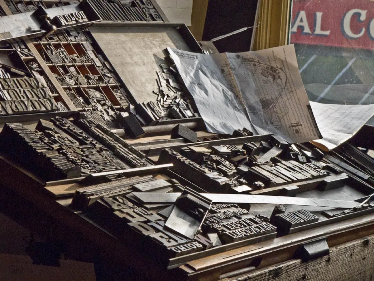 A tray of small metal type letters being set by hand in a printing works, each letter picked from its compartment and lined up in a frame.